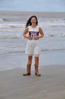 Teen in White Dress Laughing on Beach Holding Texas A&M Sign