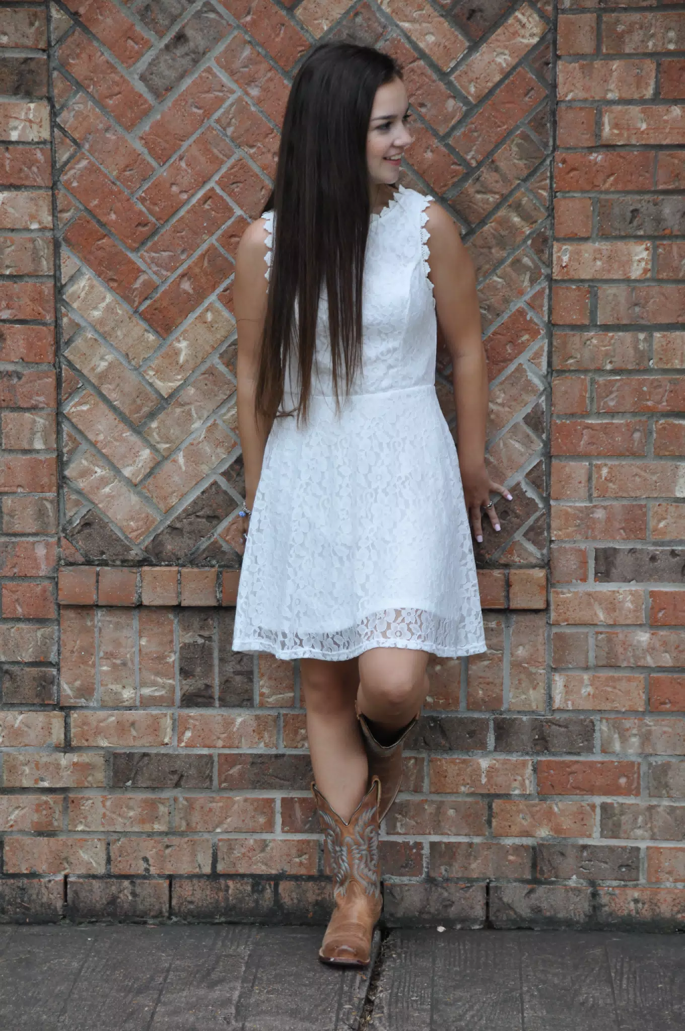 Teen Brunette Model Girl in Cowboy Boots and White Dress Against Brick Wall