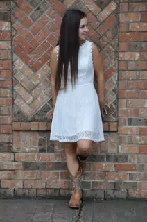 Teen Brunette Model Girl in Cowboy Boots and White Dress Against Brick Wall