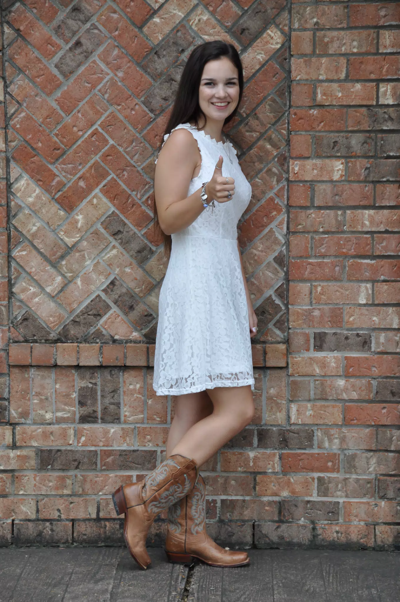 Model Thumbs Up by Brick Wall in White Dress and Cowboy Boots, Brunette