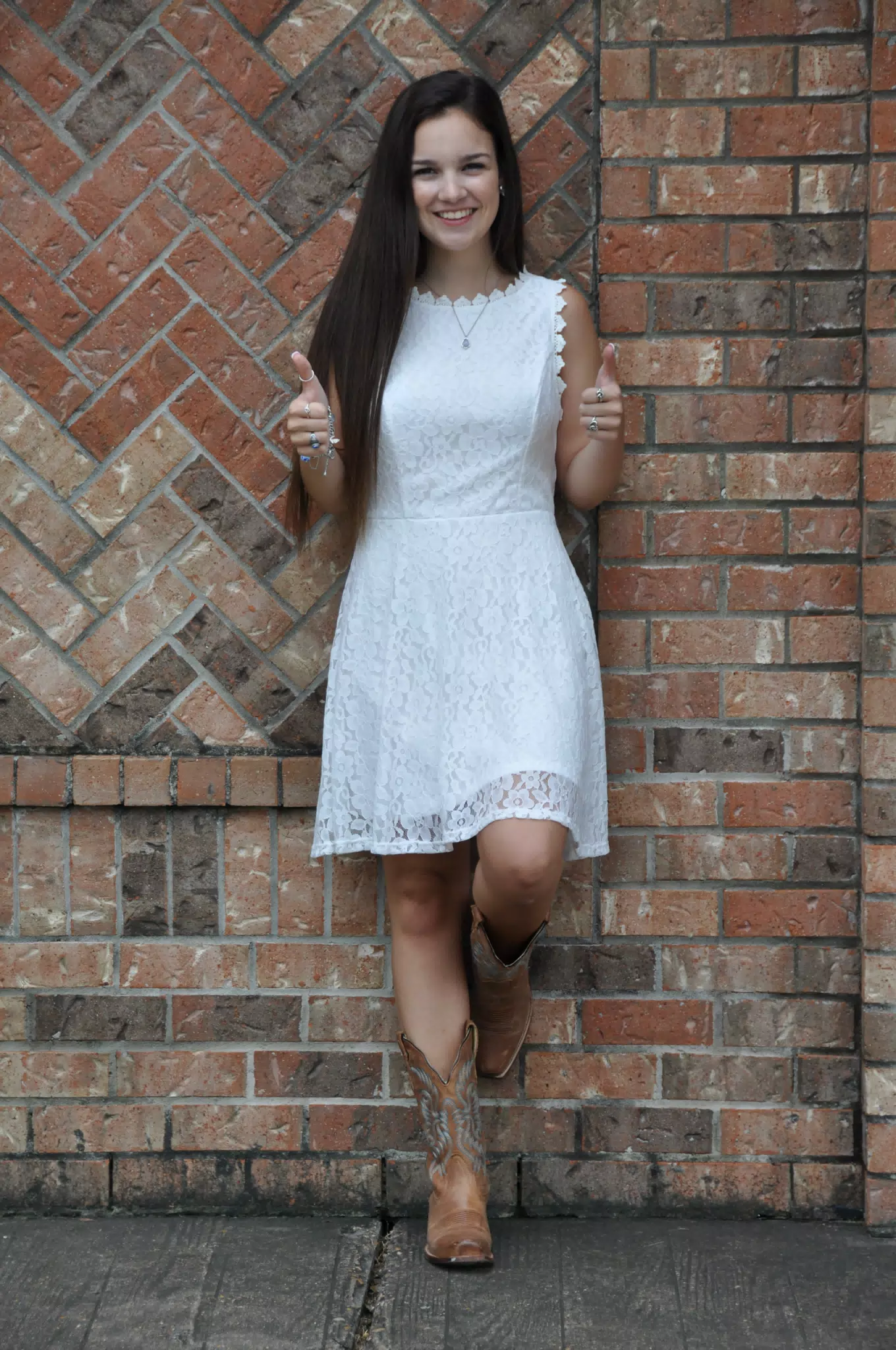 Two Thumbs Up from Teen Model in White Dress and Cowboy Boots by Brick Wall
