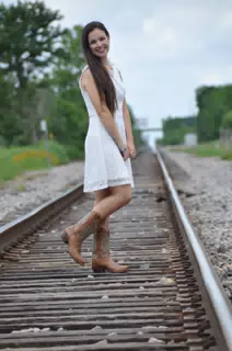 Model in White Dress and Cowboy Boots on Railroad Tracks