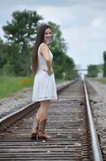 Model Looking Over Shoulder in White Dress on Railroad Tracks