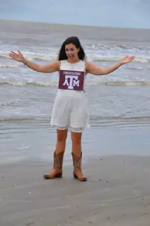 Emily with Aggies Sign in White Dress on Galveston Beach