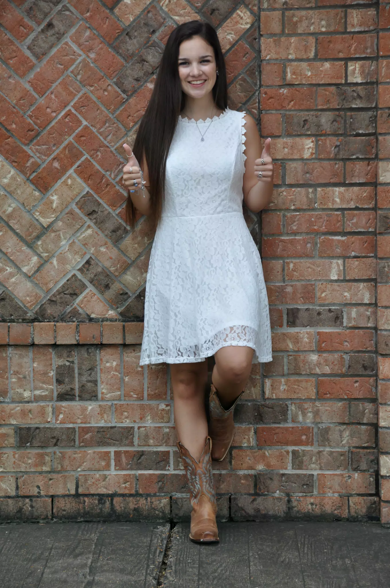 Brunette Teen Model in White Dress on Brick Wall with Cowgirl Boots Thumbs Up