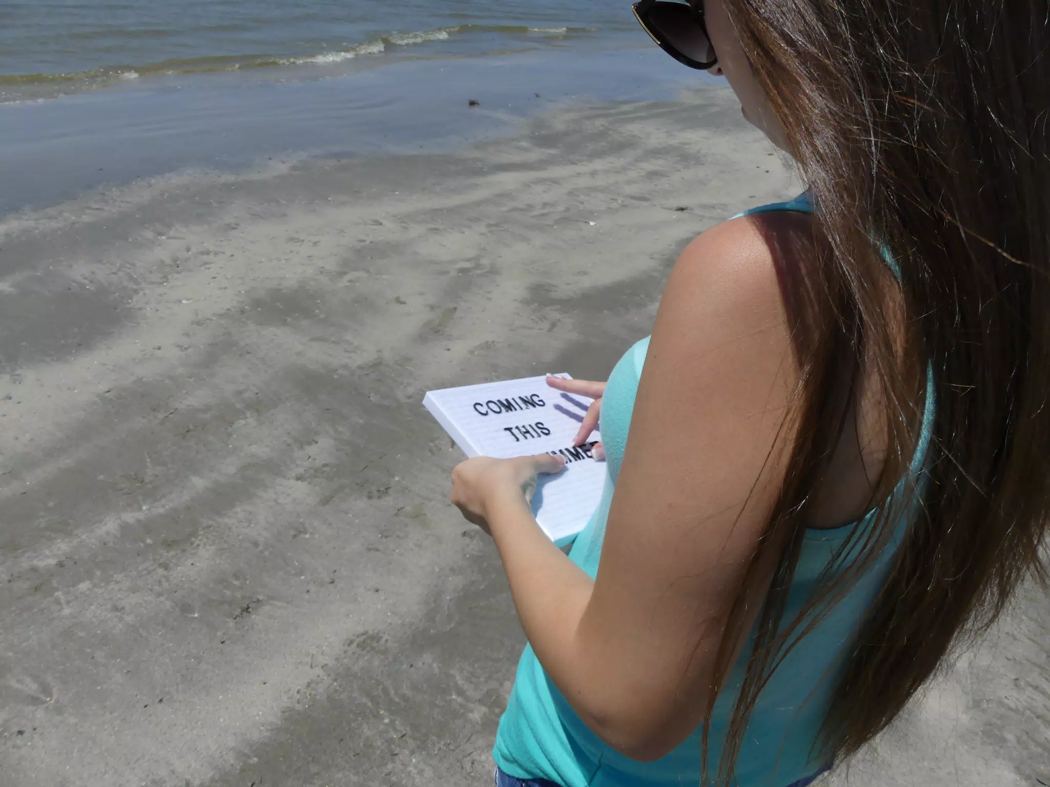Emily Making Coming This Summer Sign on Beach