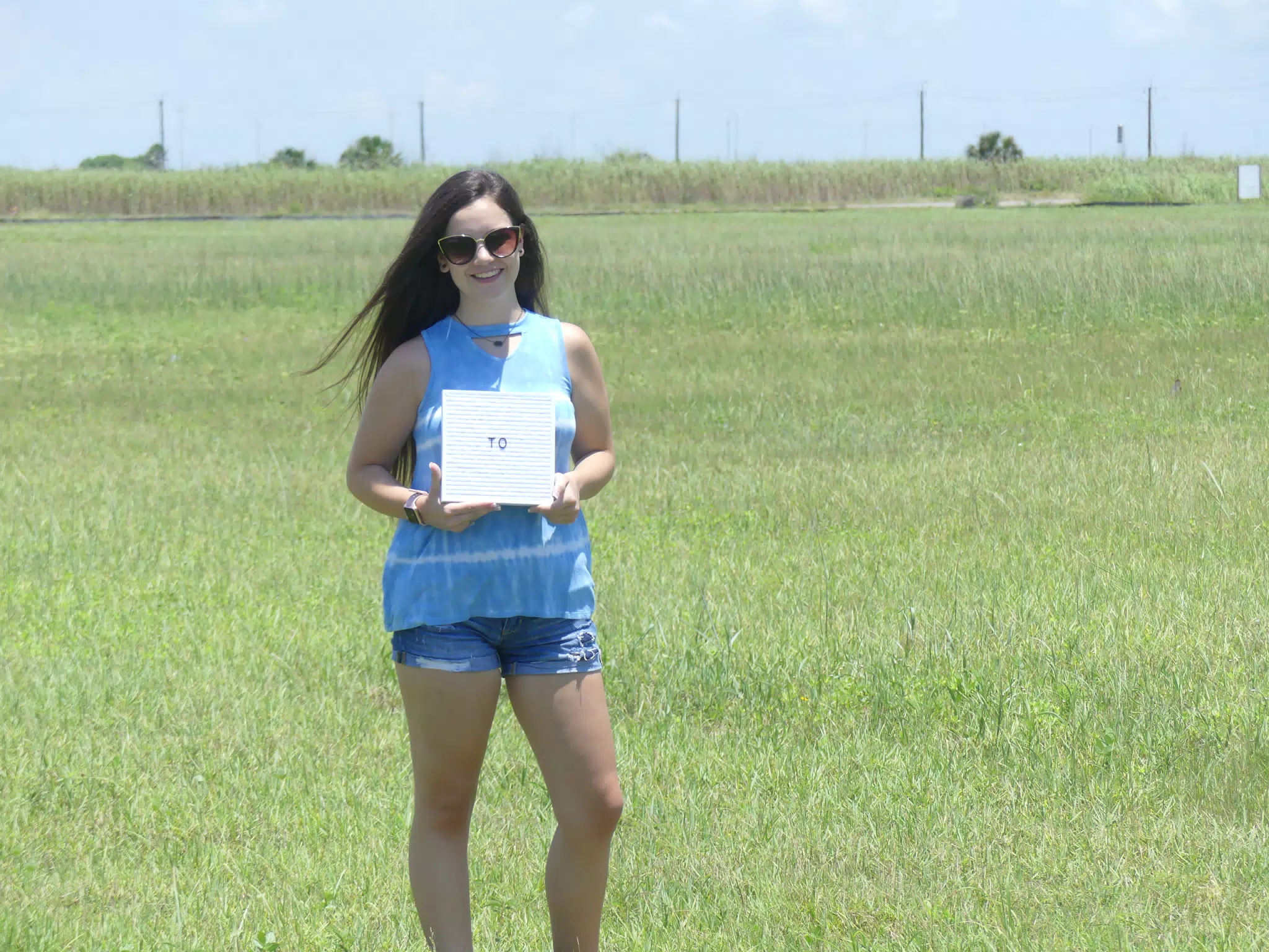 Emily with To Sign in Field on Galveston Island Near Beach in Denim Shorts
