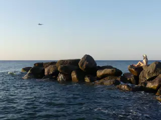 Girl Watching Airplane Land on Santorini from Beach at Sunrise