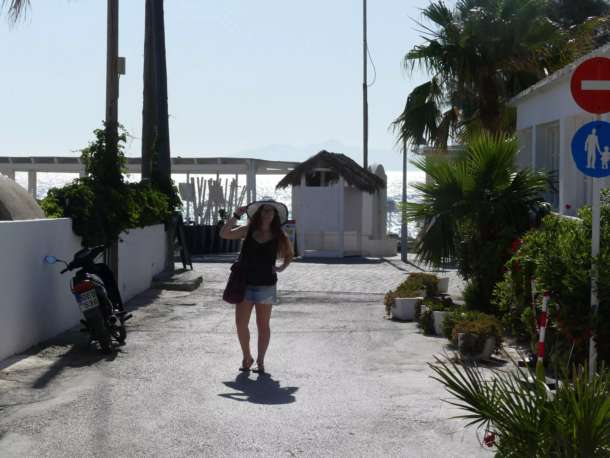 Girl with Hat on Kamari Street in Santorini by Water at Sunrise