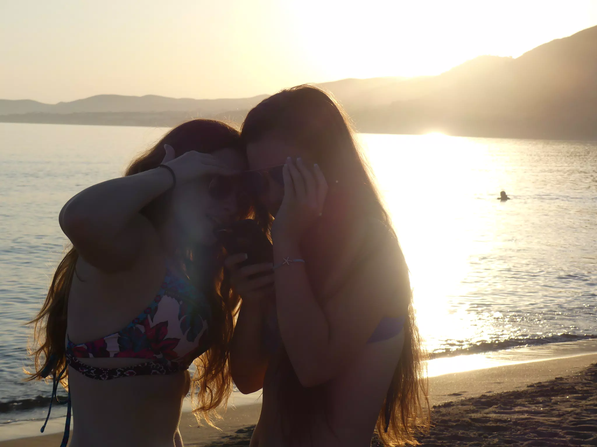 Sisters Checking Phone on Beach at Sunset in Silhouette in Palaiochora, Crete, Greece